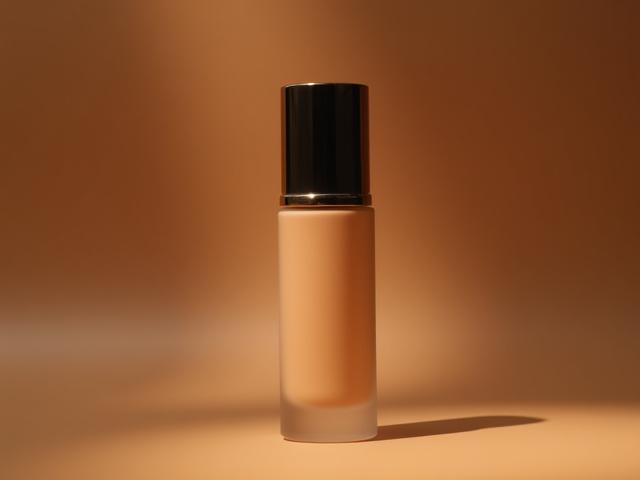 Flacone di fondotinta di lusso su sfondo sfocato di più modelli con diverse tonalità di pelle, rappresentando la versatilità del prodotto.